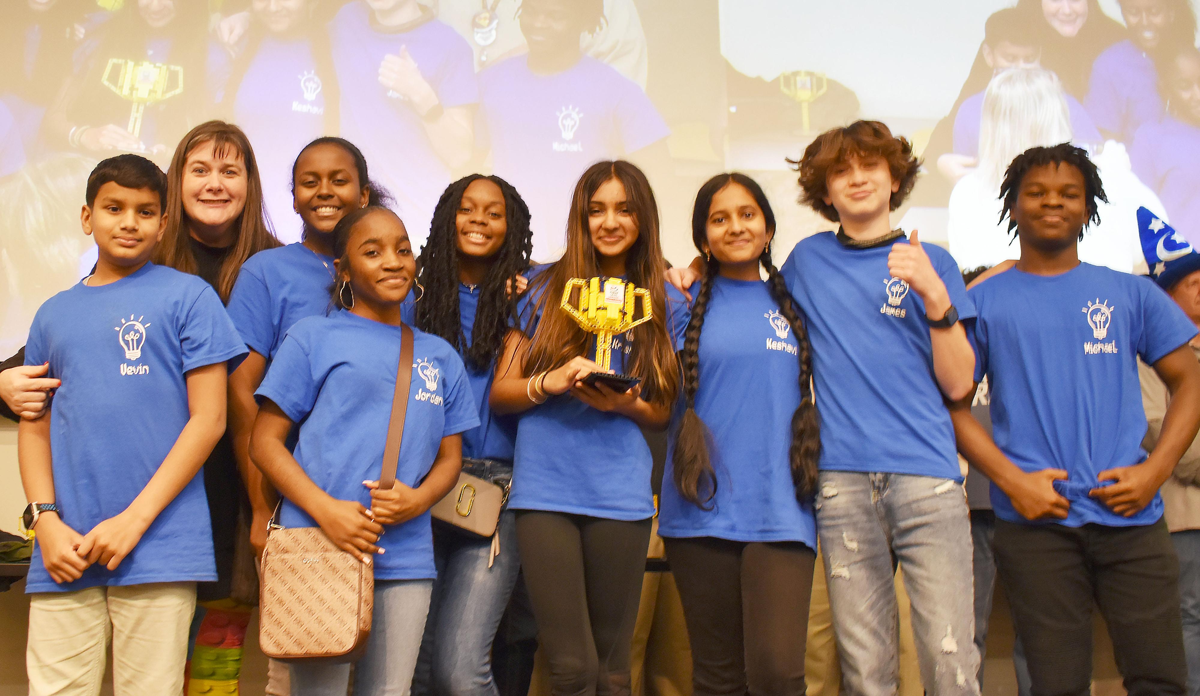 Students wearing blue shirts and posing with trophy.